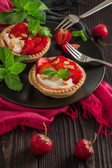 Two strawberry desserts on the basis of whipped cream in a waffle tartlet on a black plate with...