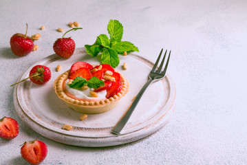 Strawberry dessert on the basis of whipped cream in a waffle tartlet with strawberries decorated with leaves of fresh mint on a white background