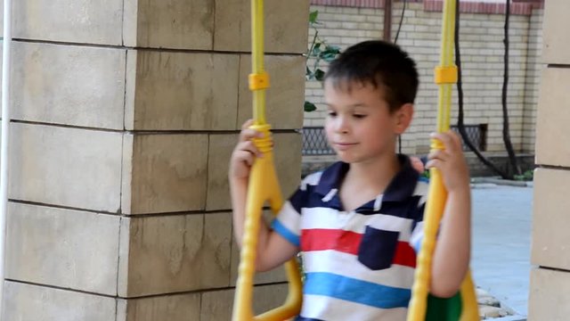 A young boy swing set in a park. The small child is having fun, smiling. It is summer time at the playground. He is wearing a t-shirt and shorts and is laughing.