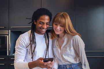 Young interracial couple laughing with the mobile