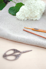 Knitting as a hobby. Metal scissors and wood crochet hook for knitting and white flowers on wood background.