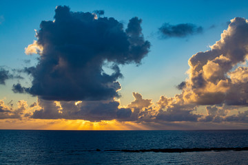 Dramatic sunset over sea water with gray clouds and sun lights