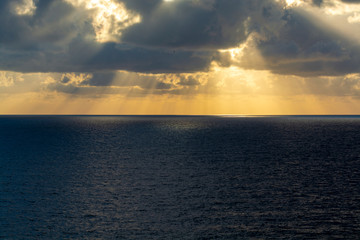 Dramatic sunset over sea water with gray clouds and sun lights
