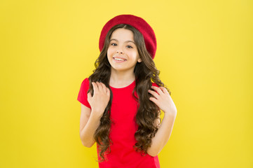 Beauty tips for tidy hair. Smiling child. Kid girl long healthy shiny hair wear red hat. Little girl with long hair. Kid happy cute face adorable curly hair yellow background. Lucky and beautiful