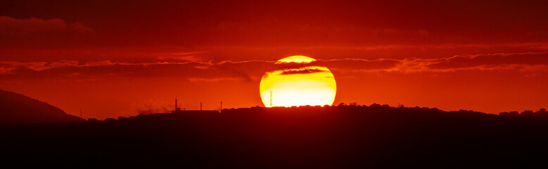 Red sun at sunset under the clouds above the horizon. Epic dramatic picture of the sky