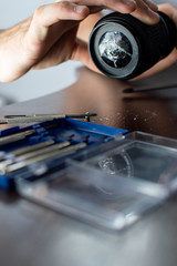 broken lens lies on the repair table with tools, close-up of a cracked lens, a man repairs photo equipment