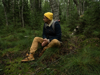 Naklejka na ściany i meble Young stylish hipster sits in woods or forest having rest and looking 