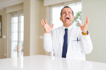 Middle age doctor man wearing medical coat at the clinic celebrating mad and crazy for success with arms raised and closed eyes screaming excited. Winner concept