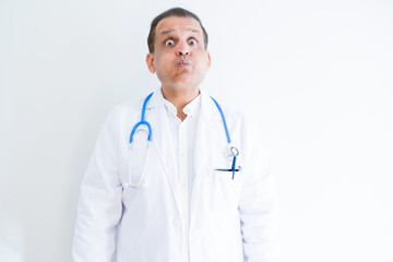 Fototapeta premium Middle age doctor man wearing stethoscope and medical coat over white background puffing cheeks with funny face. Mouth inflated with air, crazy expression.