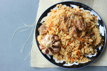 The concept of Oriental cuisine. Homemade Uzbek lamb pilaf is served on a round platter.  Copy space.