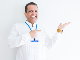 Middle age business man wearing ID card over white background amazed and smiling to the camera while presenting with hand and pointing with finger.