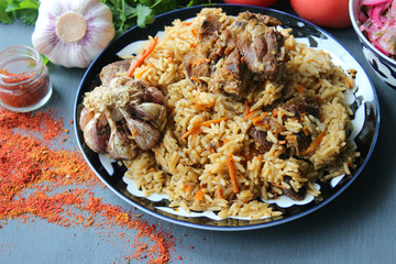 The concept of Oriental cuisine. Homemade Uzbek lamb pilaf is served on a round platter. Fresh herbs, vegetables, and spices for cooking pilaf. Copy space.