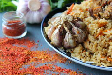 The concept of Oriental cuisine. Homemade Uzbek lamb pilaf is served on a round platter. Fresh herbs, vegetables, and spices for cooking pilaf. Copy space.