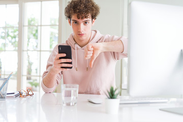 Young student man using smartphone and computer with angry face, negative sign showing dislike with thumbs down, rejection concept