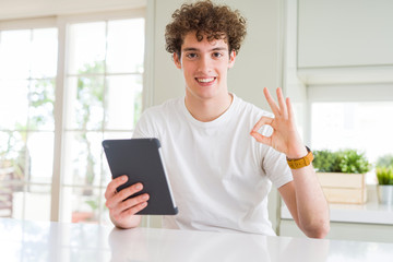 Young man using touchpad tablet doing ok sign with fingers, excellent symbol