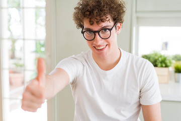 Young handsome man wearing glasses doing happy thumbs up gesture with hand. Approving expression looking at the camera showing success.