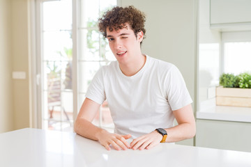 Young handsome man wearing white t-shirt at home winking looking at the camera with sexy expression, cheerful and happy face.