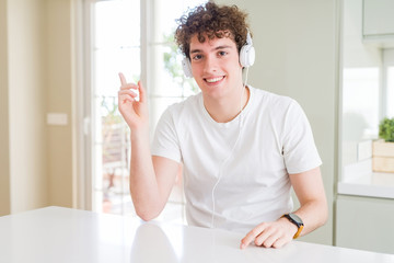 Young man listening to music wearing headphones at homes with a big smile on face, pointing with hand and finger to the side looking at the camera.