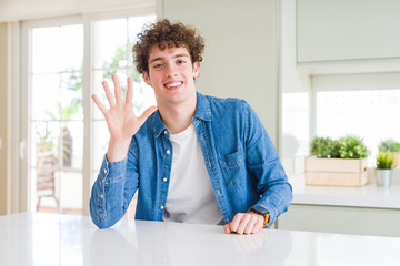 Fototapeta premium Young handsome man wearing casual denim jacket at home showing and pointing up with fingers number five while smiling confident and happy.