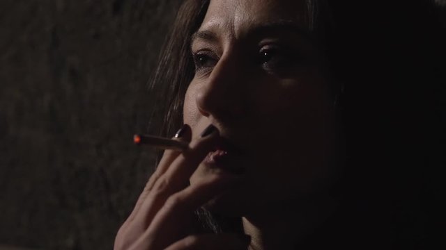 pensive sad attractive lonely woman smoking  joint  in the darkness