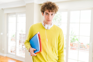 Young student man wearing headphones and holding notebooks with a confident expression on smart face thinking serious