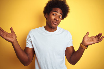 American man with afro hair wearing white t-shirt standing over isolated yellow background clueless...