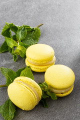 French macaroons isolated. Selective focus. Beautiful yellow macaroons with mint on gray stone background. Stylish arrangement sweet. Flat lay, top view. Macro photo.