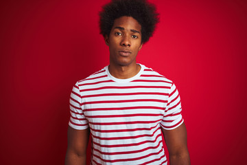 Fototapeta na wymiar Young african american man with afro hair wearing striped t-shirt over isolated red background Relaxed with serious expression on face. Simple and natural looking at the camera.