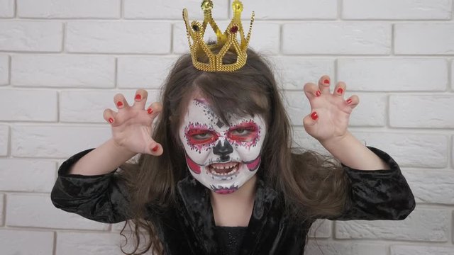 Horror at Halloween day. A little girl in scary makeup and a crown scares the camera. Halloween child.