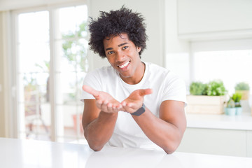 Young african american man wearing casual white t-shirt sitting at home Smiling with hands palms together receiving or giving gesture. Hold and protection