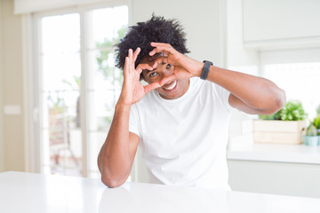 Young african american man wearing casual white t-shirt sitting at home Doing heart shape with hand and fingers smiling looking through sign