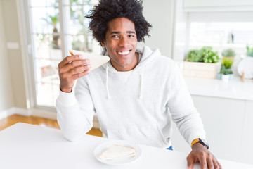 Fototapeta na wymiar African American man eating handmade sandwich at home with a happy face standing and smiling with a confident smile showing teeth