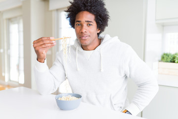 Fototapeta na wymiar African American man eating asian noodles using chopsticks at home with a confident expression on smart face thinking serious