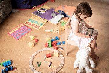 Girl Plays Mobile Phone. The Girl is Hooked to the Mobile Phone. He does not play with toys. The mobile phone is bad for children.