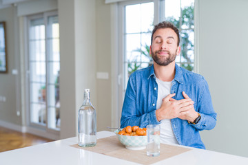 Handsome man eating pasta with meatballs and tomato sauce at home smiling with hands on chest with closed eyes and grateful gesture on face. Health concept.