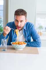Handsome man eating pasta with meatballs and tomato sauce at home while smiling at the camera