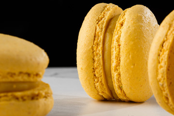 French macaroons isolated. Selective focus. Beautiful yellow macaroons on marble and dark background. Stylish arrangement sweet. Flat lay, top view. Macro photo.