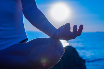 Woman is practicing yoga sitting in Lotus pose at sunrise. Silhouette of woman meditating on the...