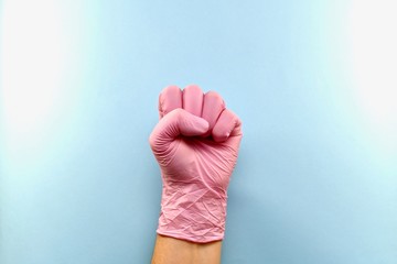 The left hand, clenched into a fist with the inner side. In pink medical rubber gloves on a blue...