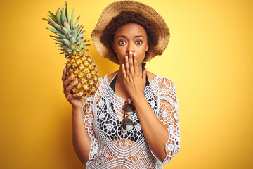 Young african american woman with afro hair holding pineaple over yellow isolated background cover...