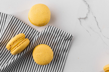 French macaroons isolated. Selective focus. Beautiful yellow macaroons in striped napkin on marble background. Stylish arrangement sweet. Flat lay, top view. Macro photo. With copy space.