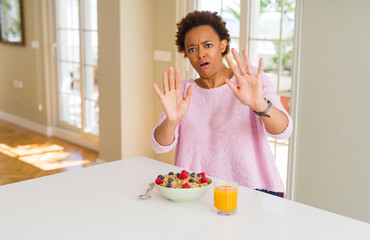 Young african american woman having healthy breakfast in the morning at home afraid and terrified with fear expression stop gesture with hands, shouting in shock. Panic concept.