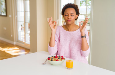 Young african american woman having healthy breakfast in the morning at home relax and smiling with eyes closed doing meditation gesture with fingers. Yoga concept.