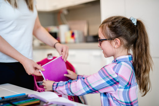 Mother helping her daughter in packing school bag.