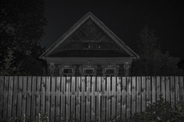 Old abandoned wooden house and fence in front of him in the village at sunset Russia