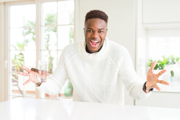African american man driking a fresh glass of water very happy and excited, winner expression celebrating victory screaming with big smile and raised hands