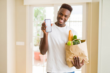 African man holding a paper bag full of groceries and using smarpthone buying online using app smiling
