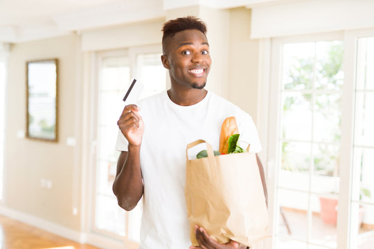African american man holding paper bag full of groceries and holding credit card as payment