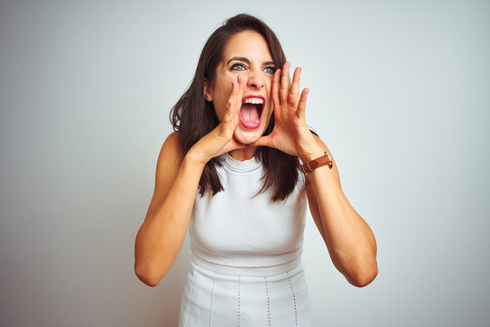 Young beautiful woman wearing dress standing over white isolated background Shouting angry out loud with hands over mouth