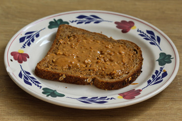 Bread with peanut butter on white plate on wooden background